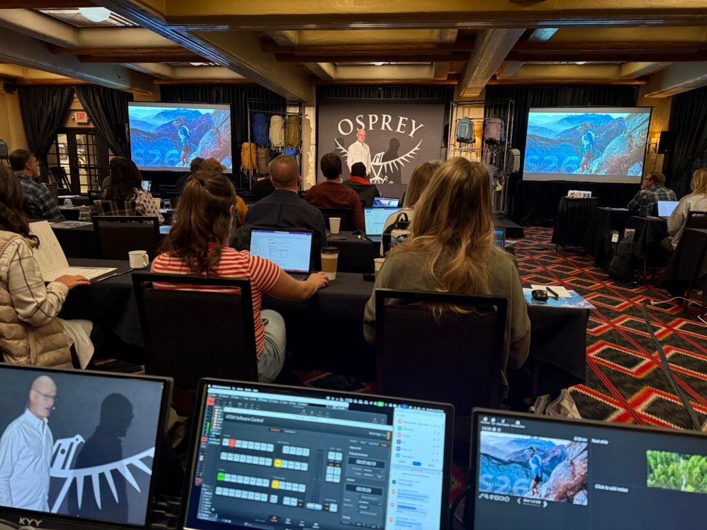 Hand in Hand Productions managing live production at an Osprey corporate event, with audience, large LED screens, and ATEM switching software running in the foreground